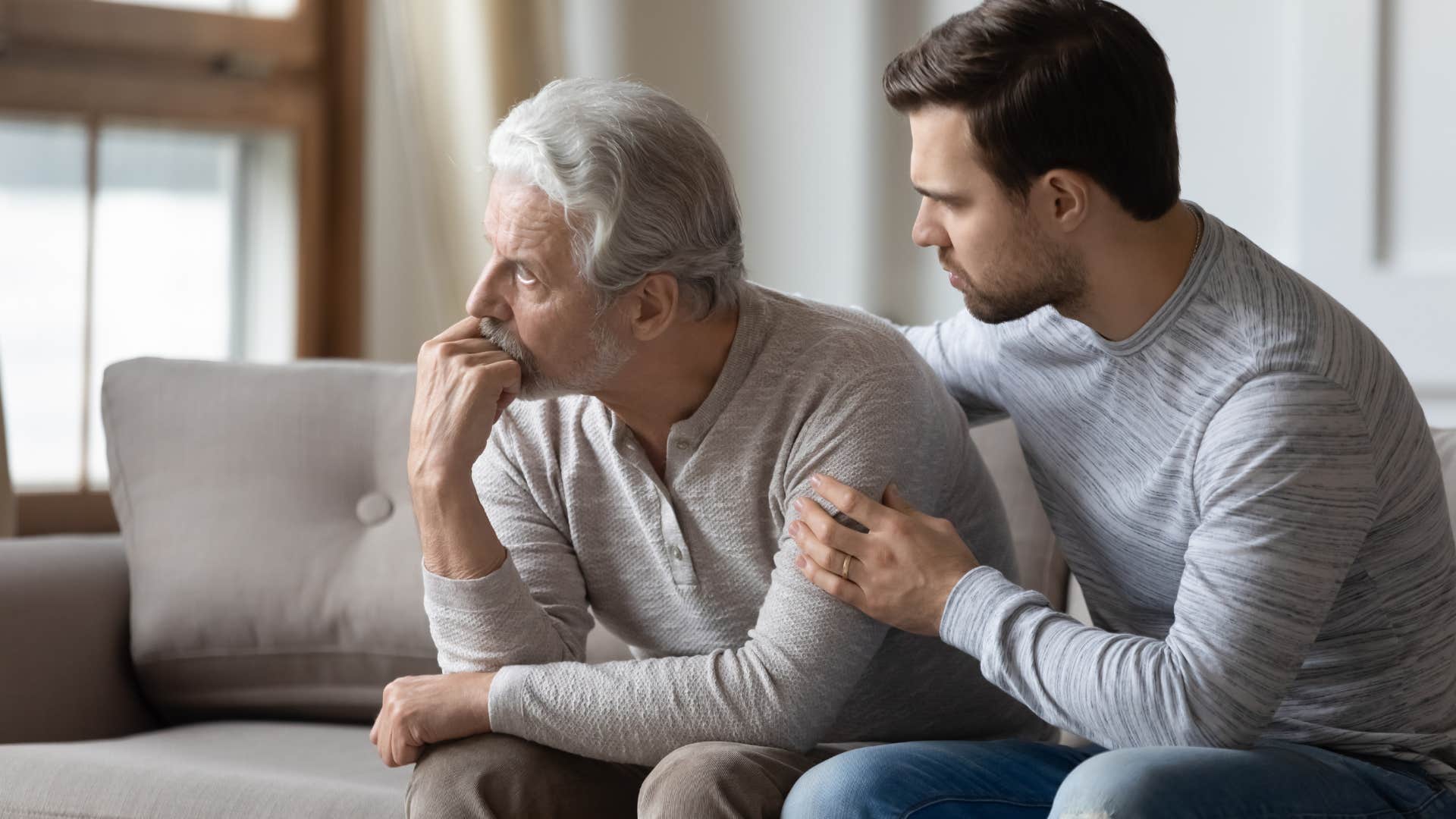 Adult son comforting his dad on the couch