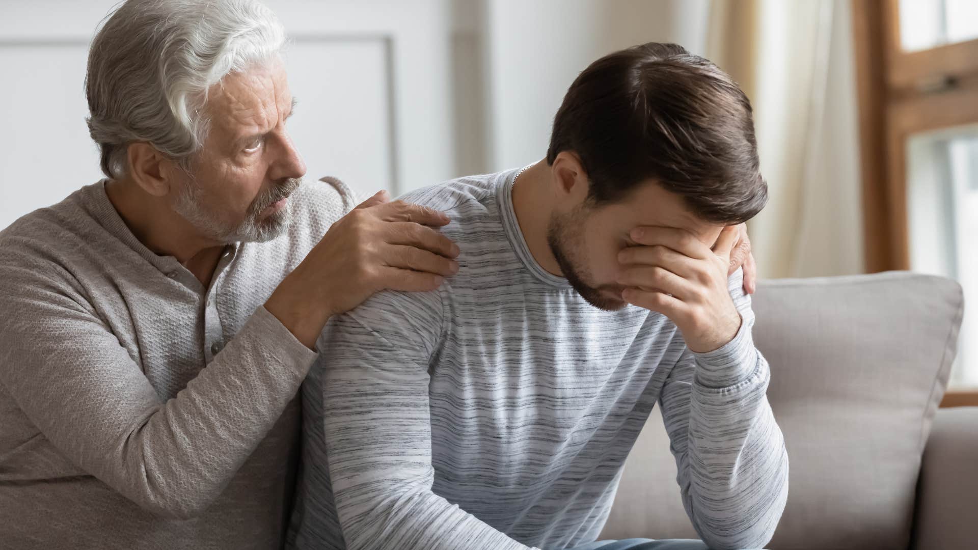 Adult man looking upset being comforted by his dad