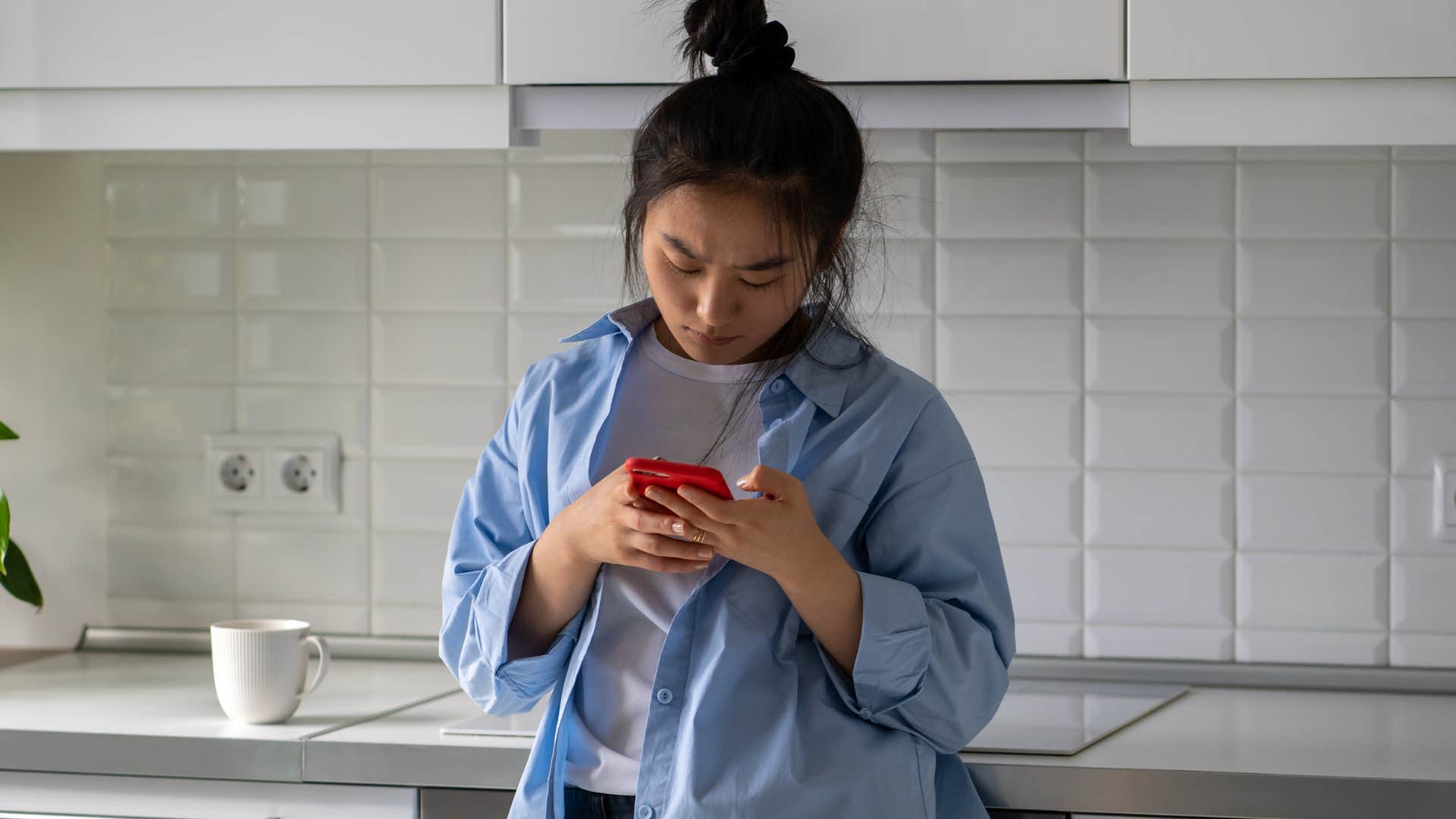 Woman looking annoyed staring at her phone in the kitchen