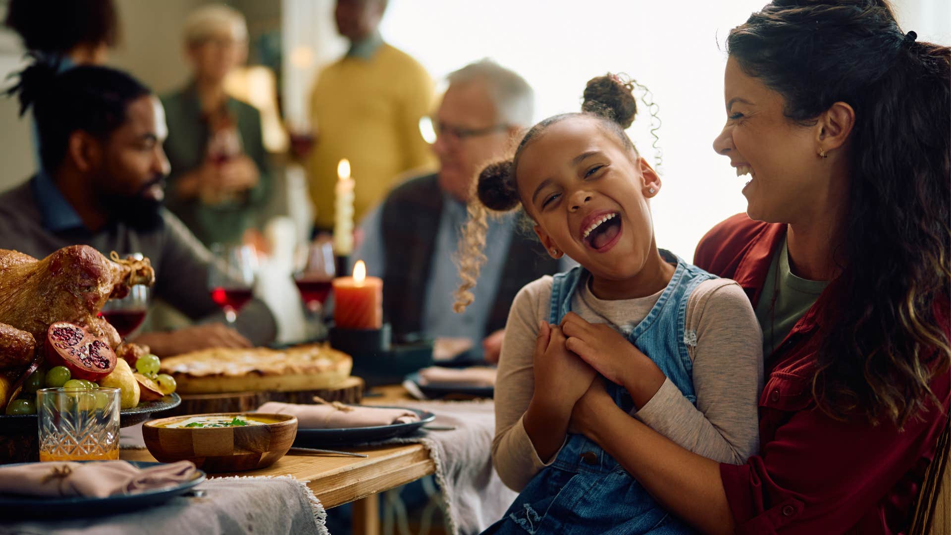 Woman holding her smiling daughter at a holiday dinner.