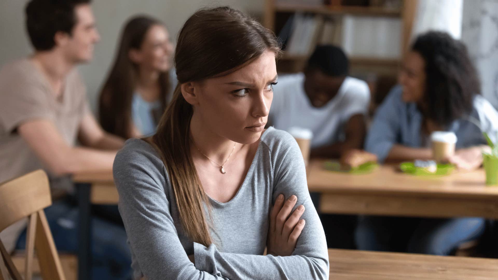 woman looking upset while group of people talk behind her 