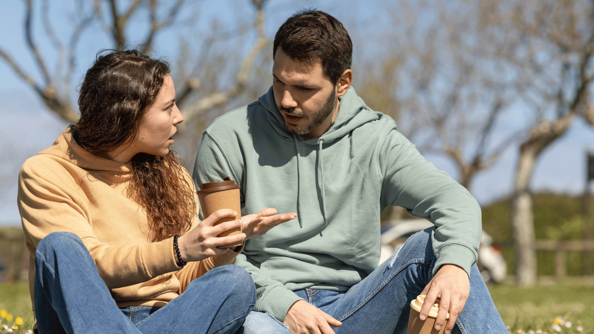 man and woman sitting down on grass arguing 