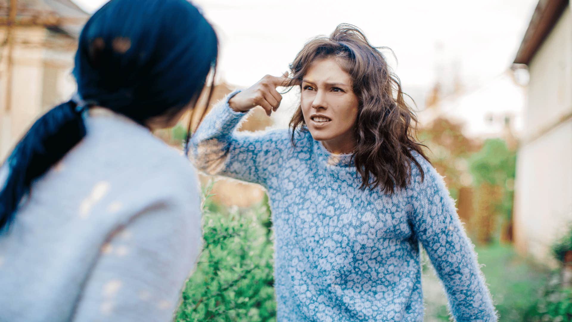 woman yelling at another woman outside while pointing at her head 