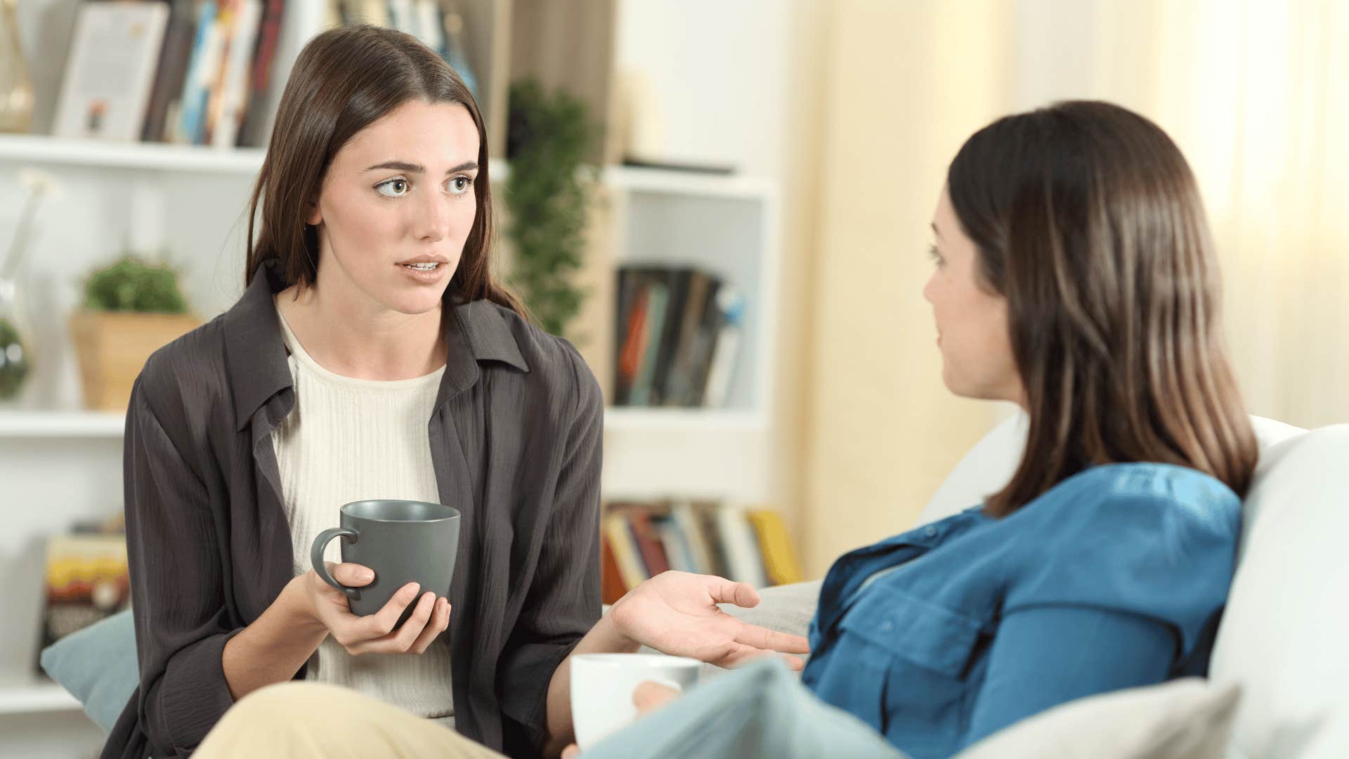 two women discussing on the couch while drinking hot drink