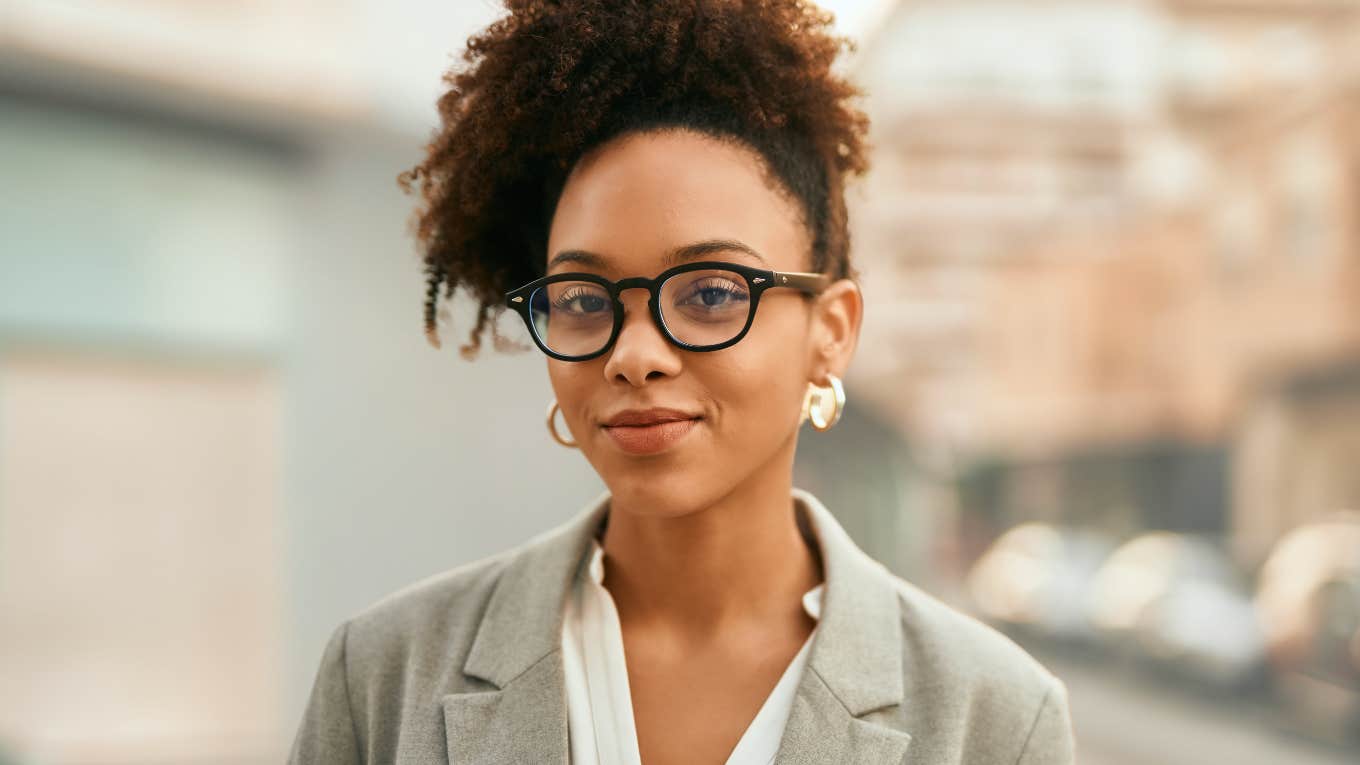 Woman wearing glasses smiling at the camera in professional clothing.