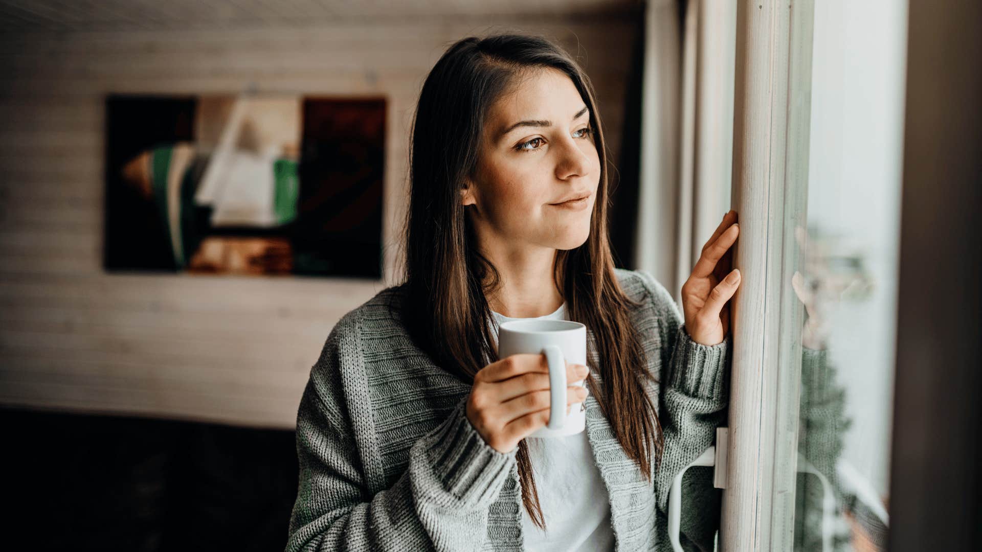 woman holding cup while looking out of window