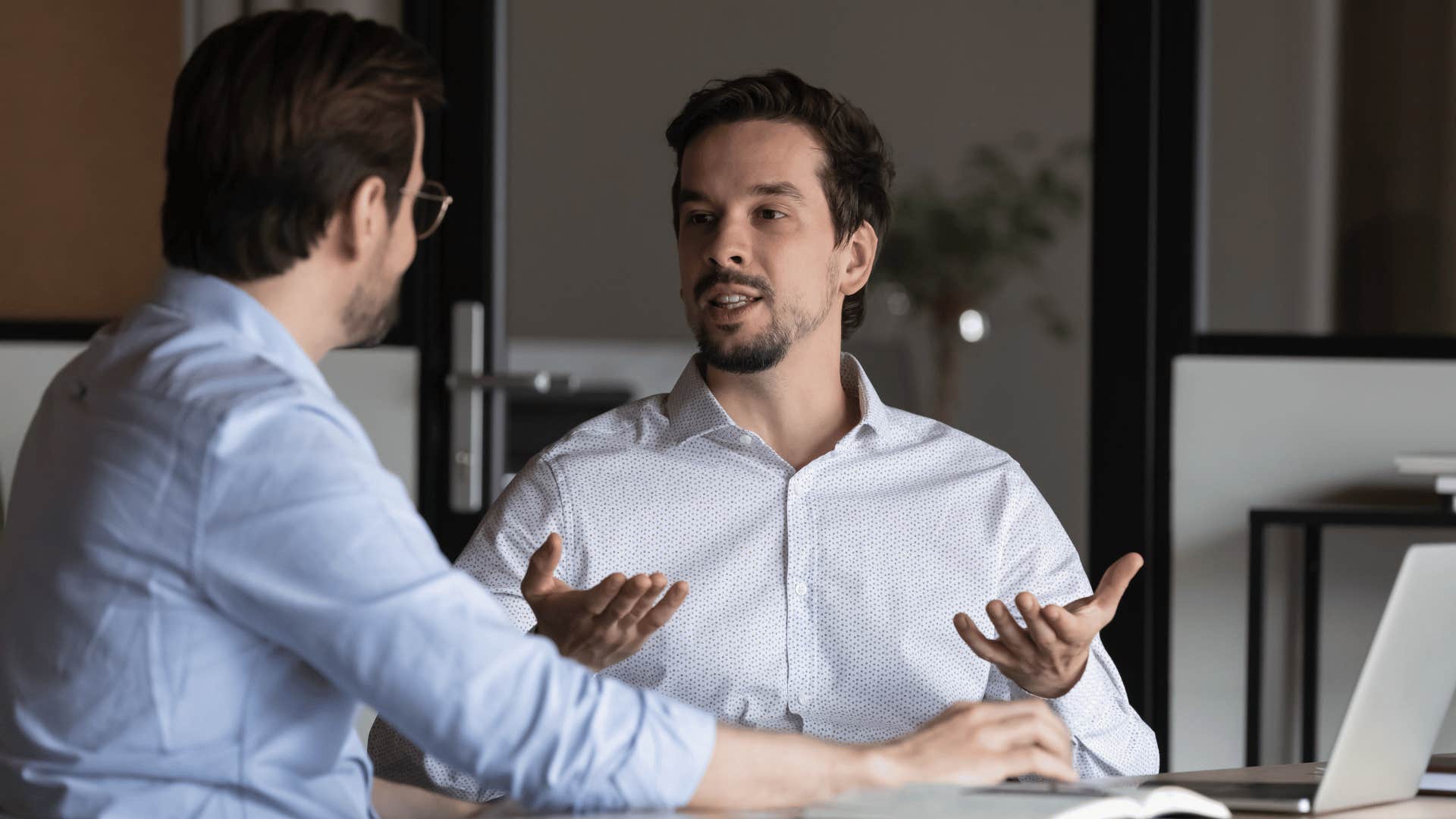 two men talking while one man holds his hands up