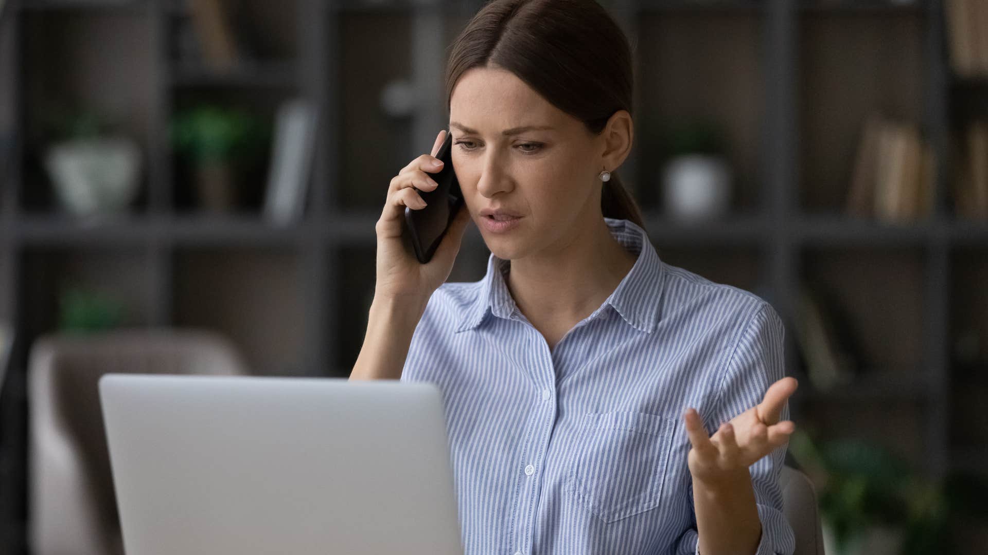 Woman looking annoyed while talking on the phone and looking at her laptop.