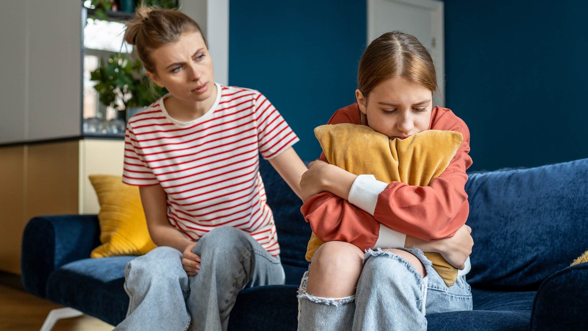 Mother comforting her upset younger daughter on the couch.