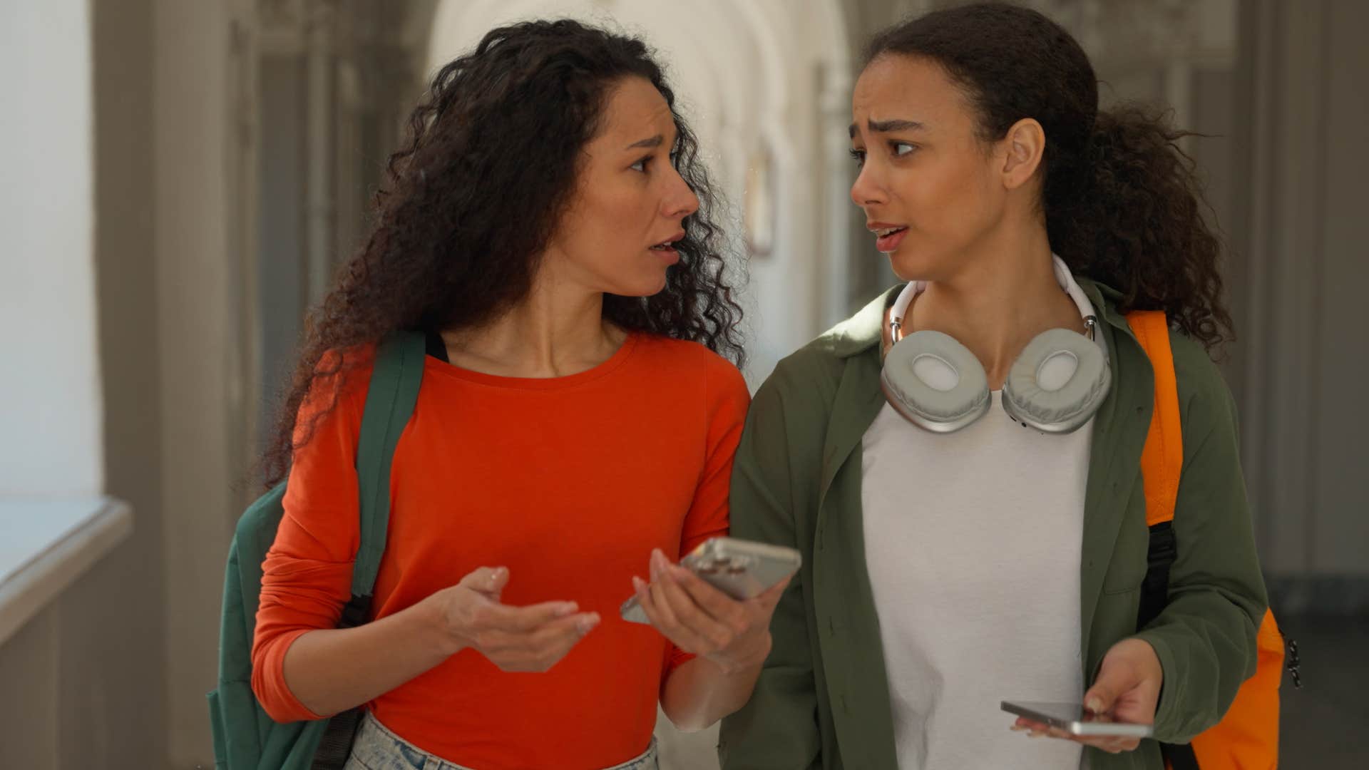 Two young women walking and talking together looking upset.