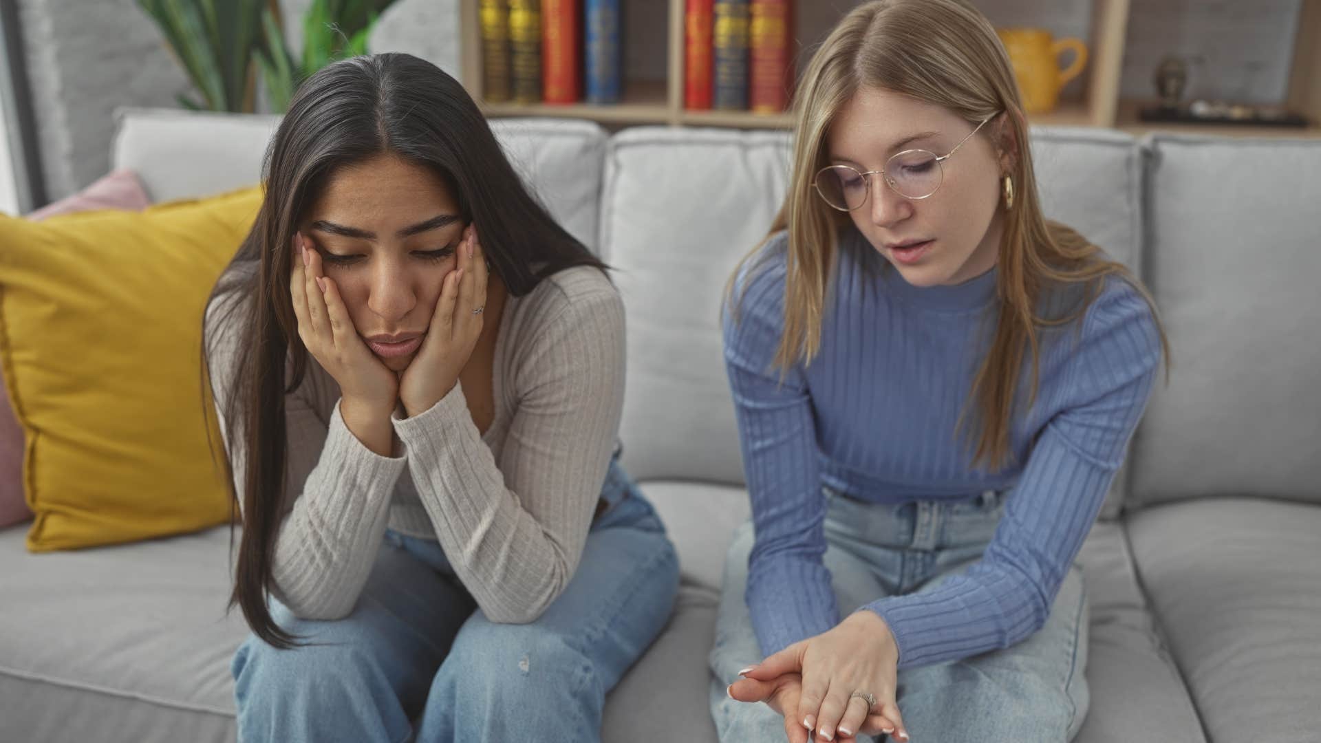 Two young women looking upset sitting on the couch together.