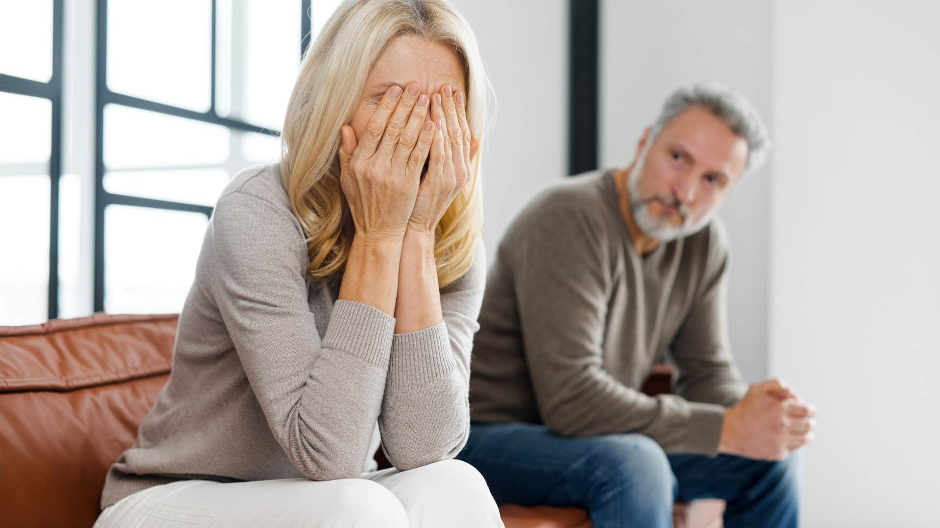 Older woman holding her face in her hands next to her husband