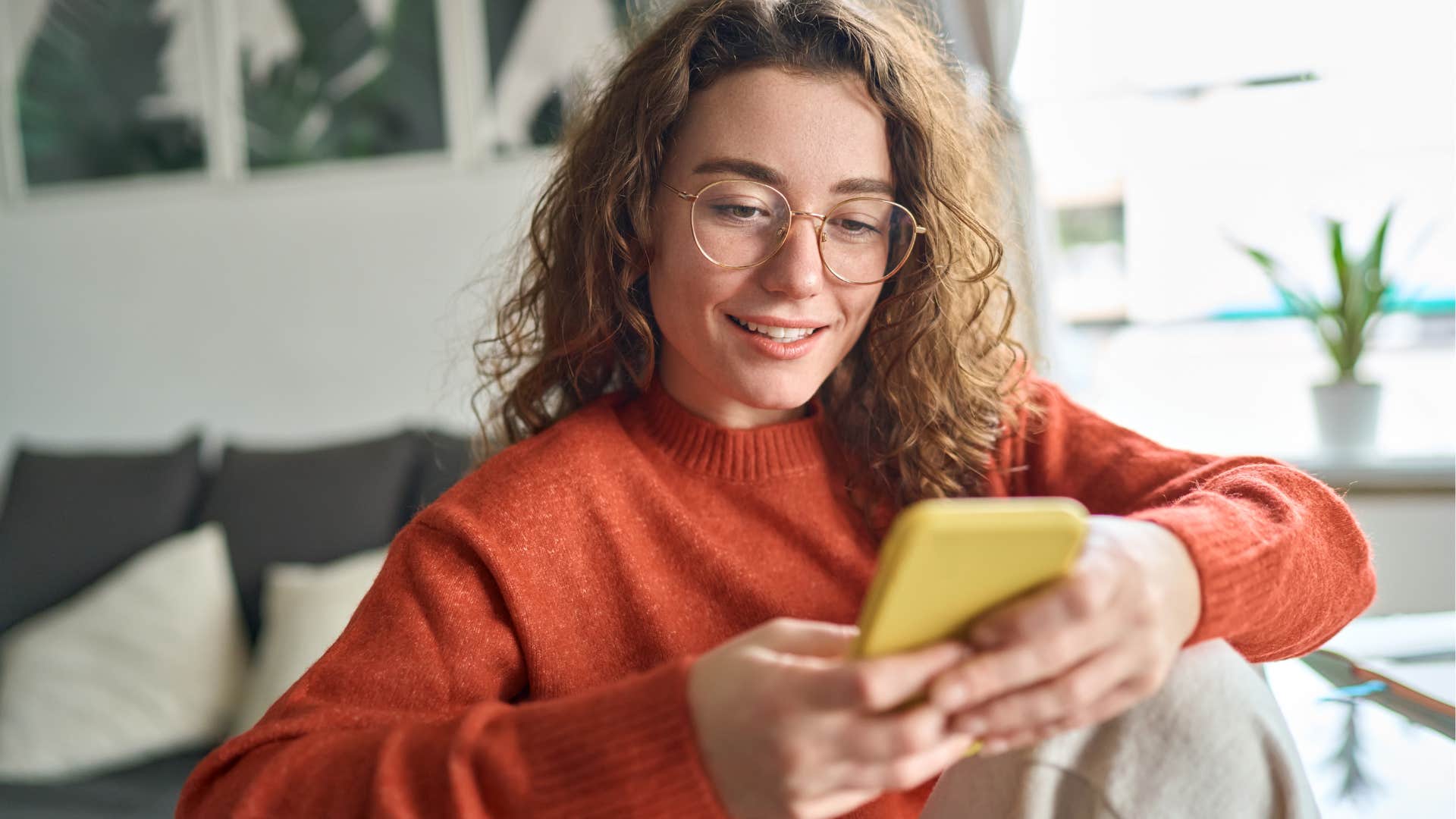 Young woman smiling while scrolling on her cell phone.