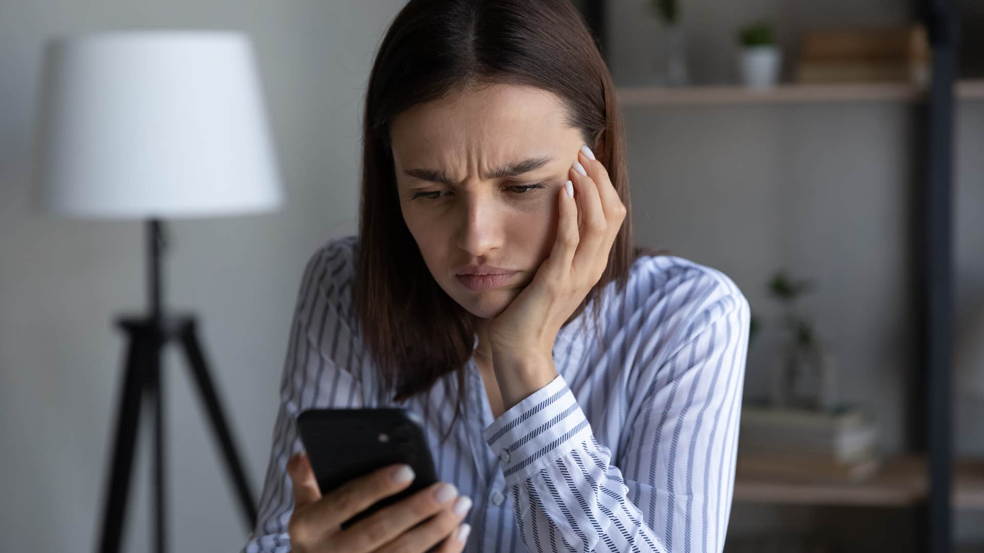 Woman holding her chin while staring at her cell phone.