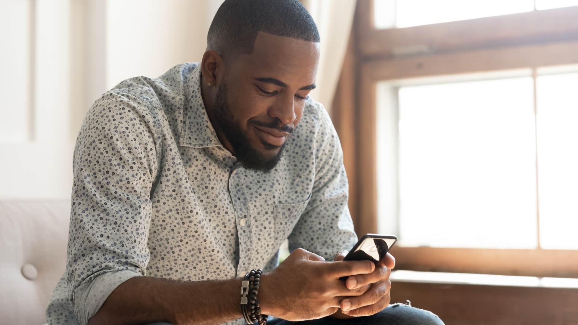 Man smiling while texting on his phone.