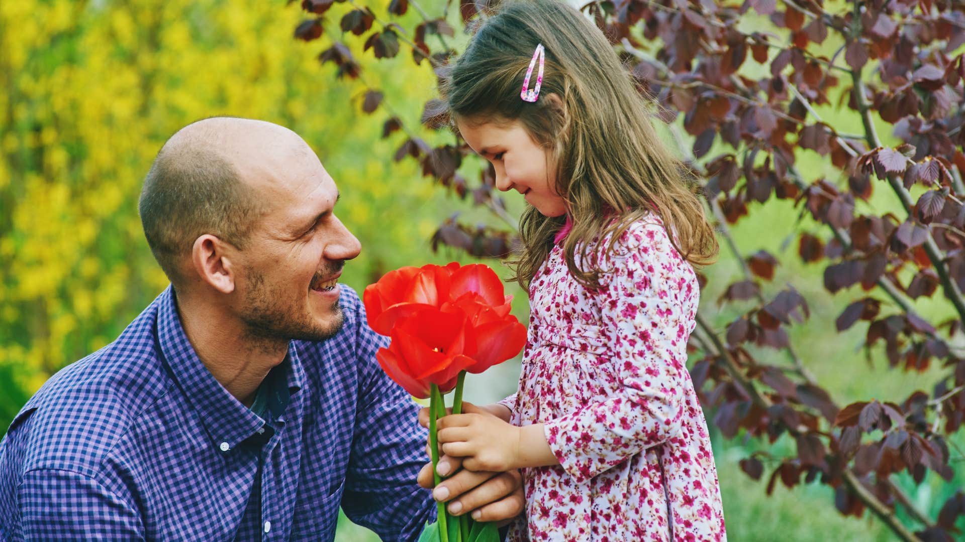 Dad holding a flower to his smiling daughter.