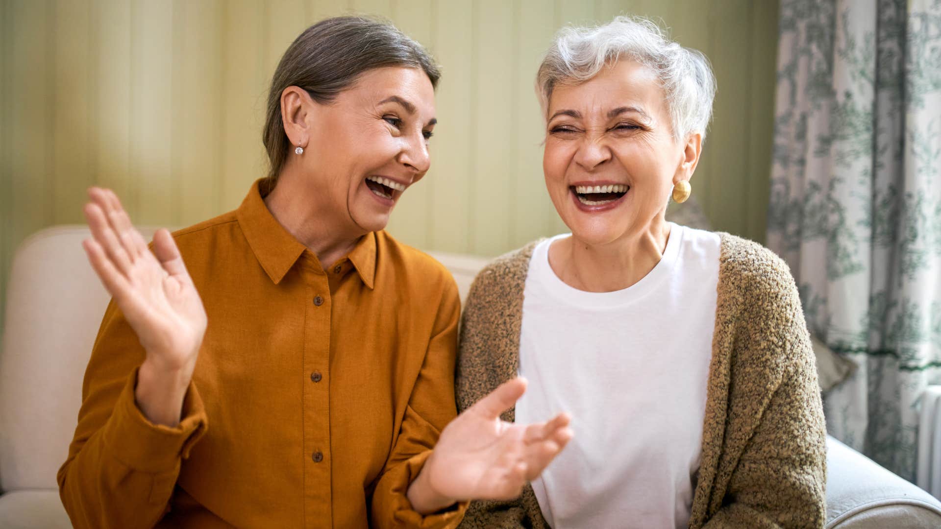 Two older women smiling and sitting next to each other.