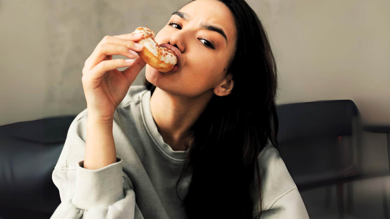 Woman eating a sugary donut at home, contributing to her anxiety. 