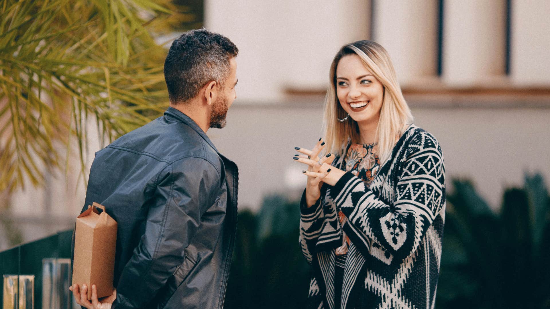 man talking to woman hiding present behind him