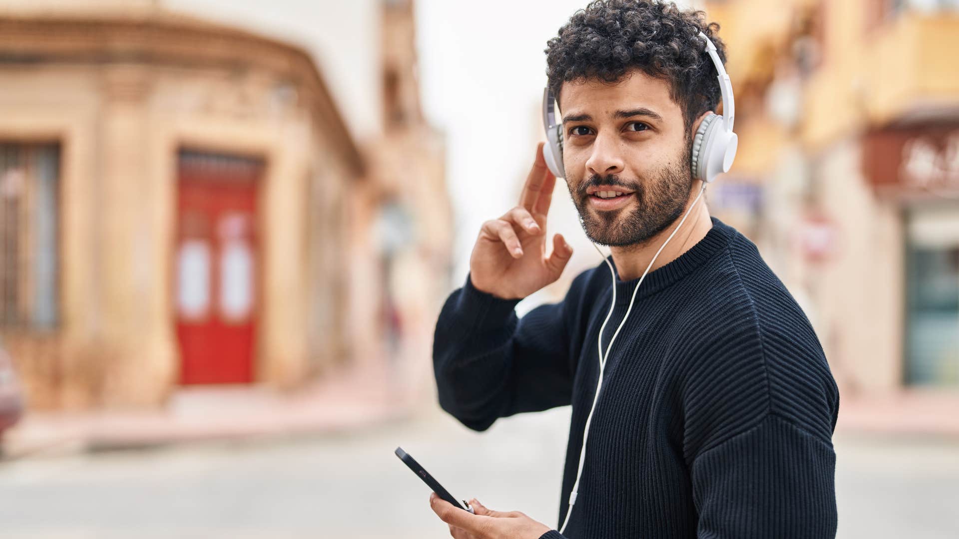 Man smiling and walking outside with his headphones on.