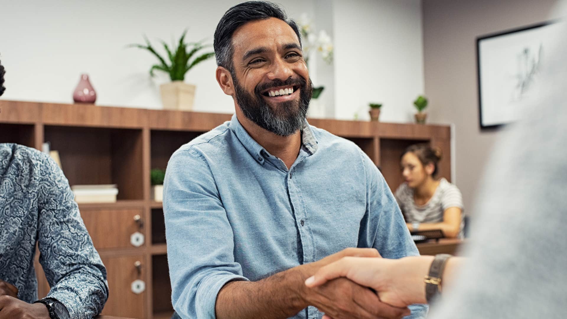 Man smiling and shaking another person's hand.