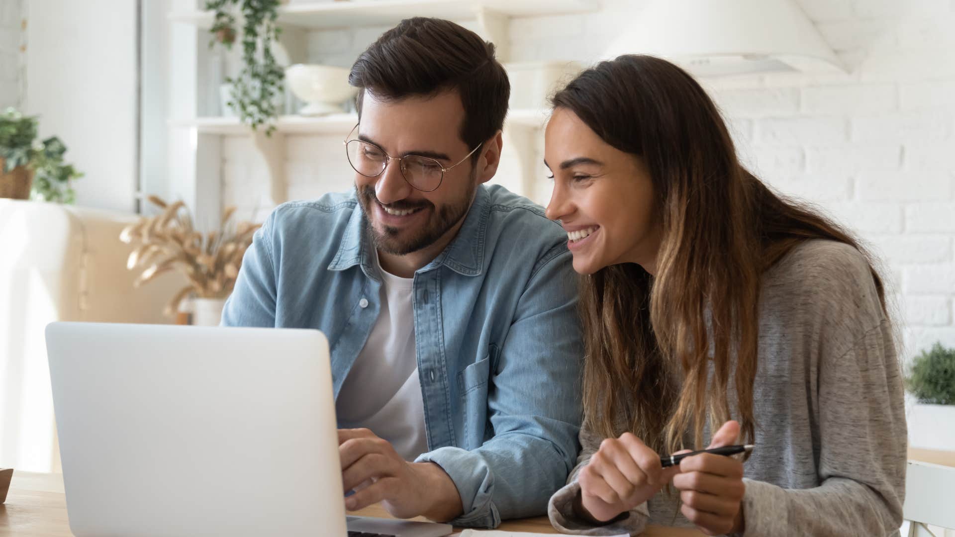 Man and woman smiling while looking at a laptop together.