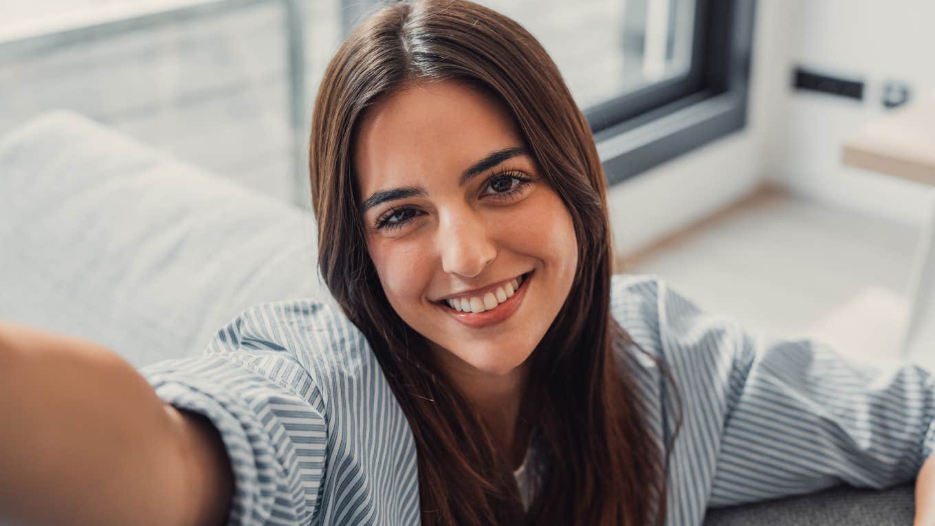 Happy young adult woman sitting on sofa looking at camera in modern cozy home