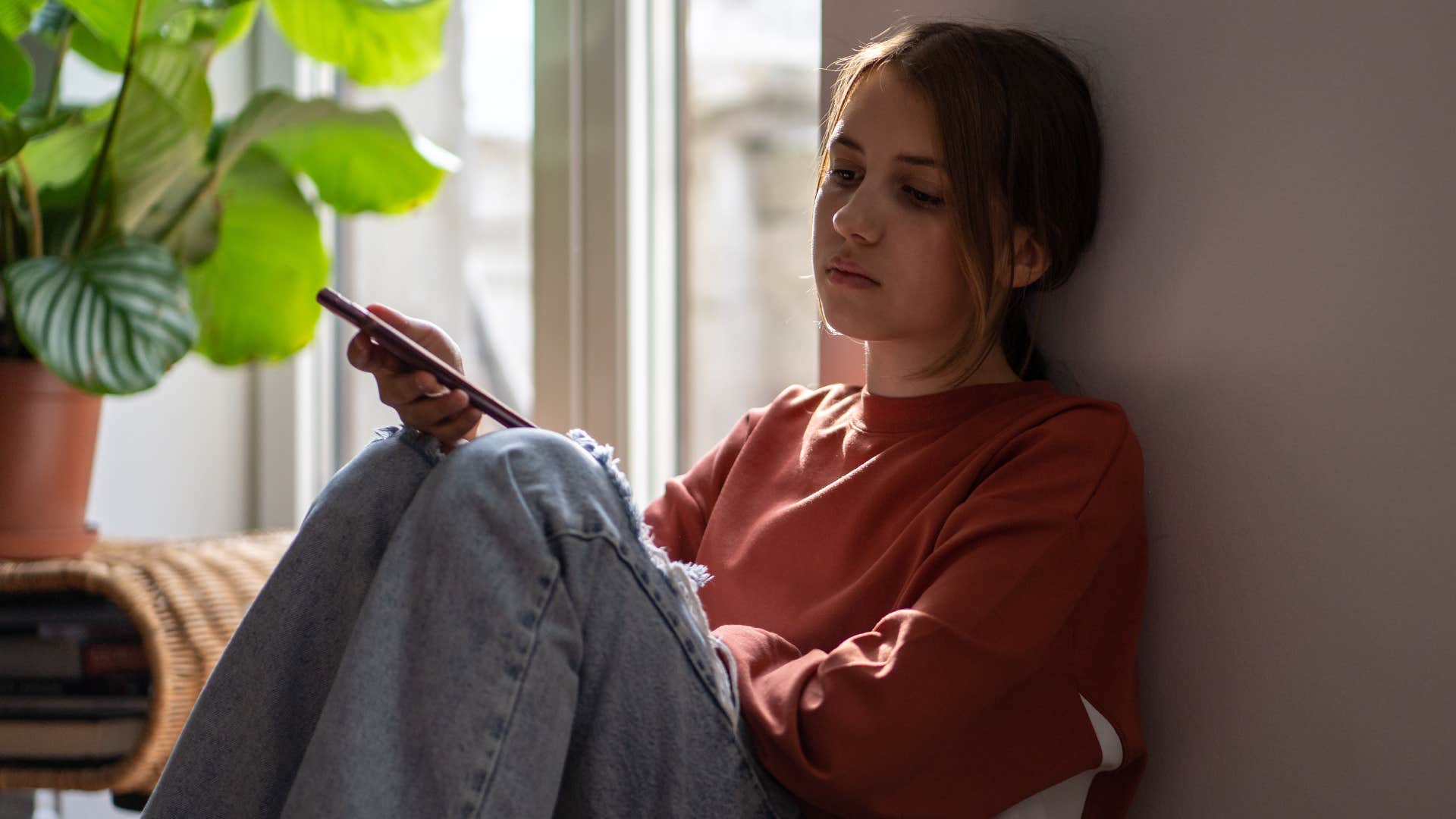 Teenage girl looking sad while holding her phone.