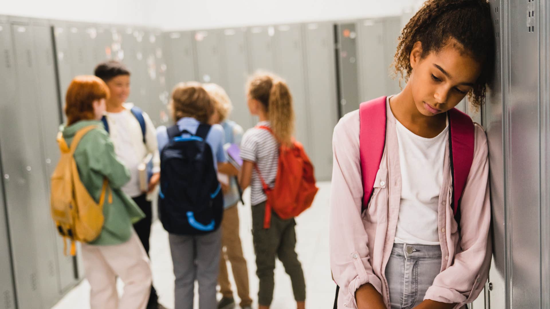 Teenager looking sad while leaning against her school locker.