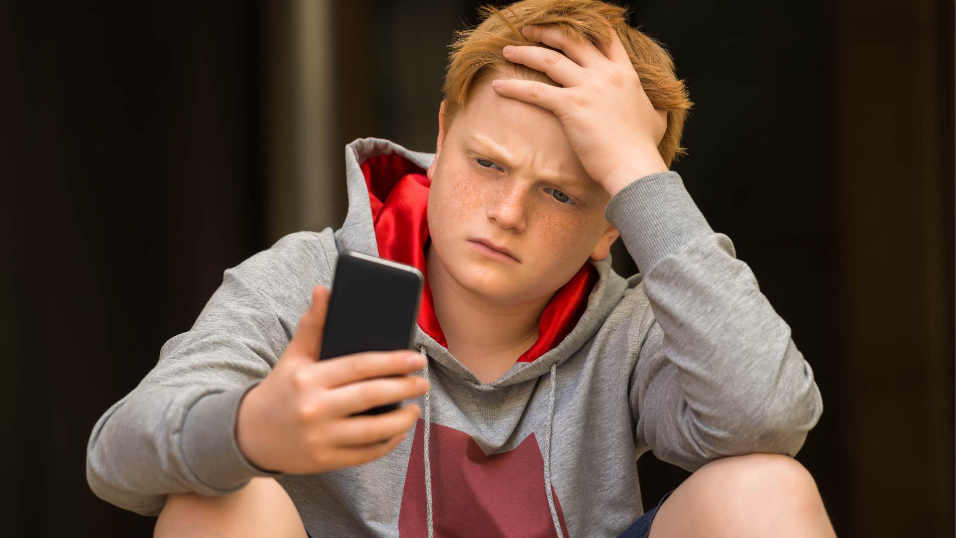 Teenage boy looking confused staring at his phone.