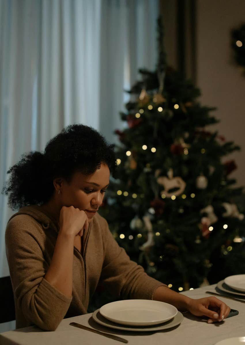 sad woman sitting by herself next to Christmas tree