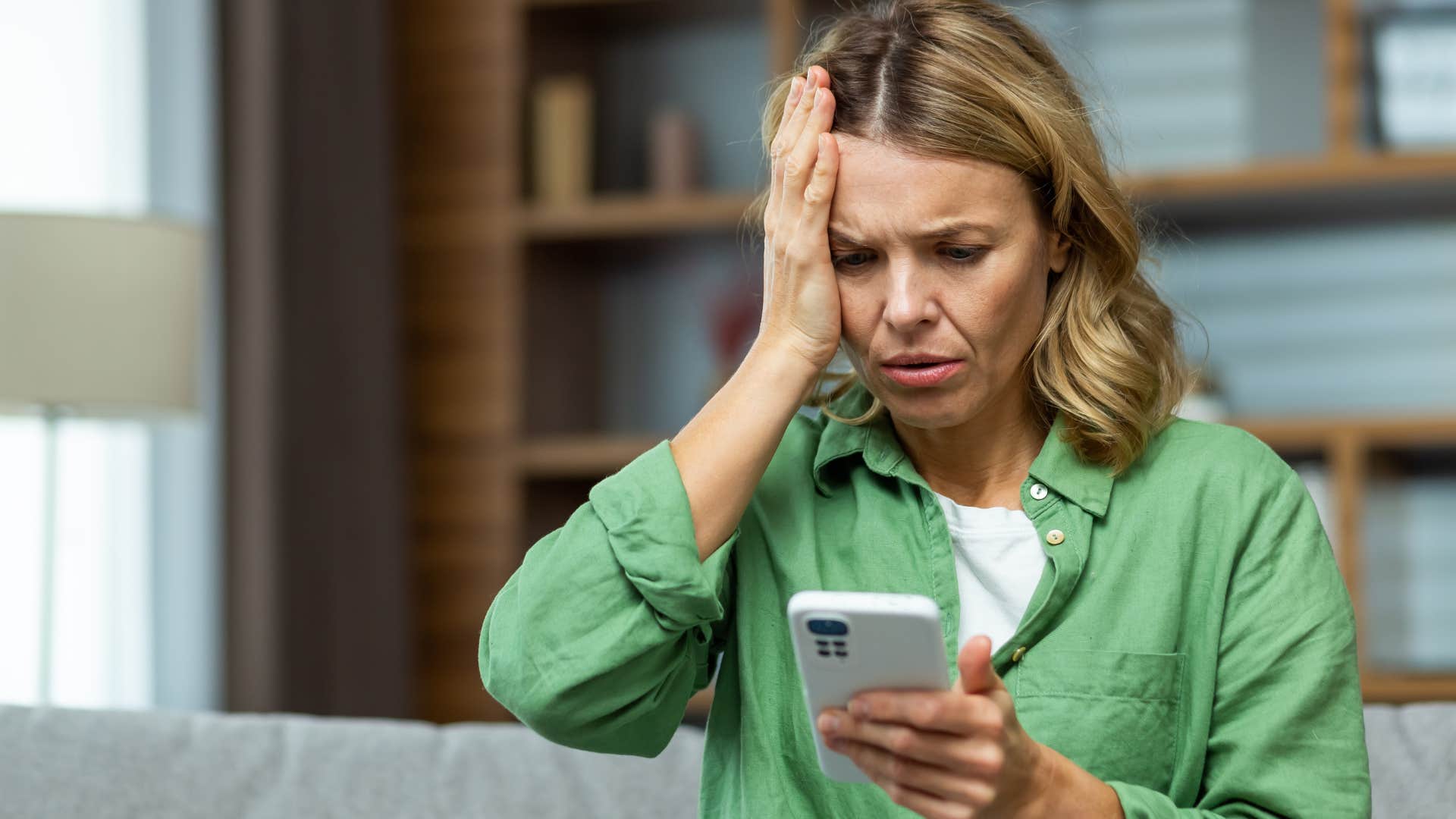 Woman holding head looking upset at her phone. 