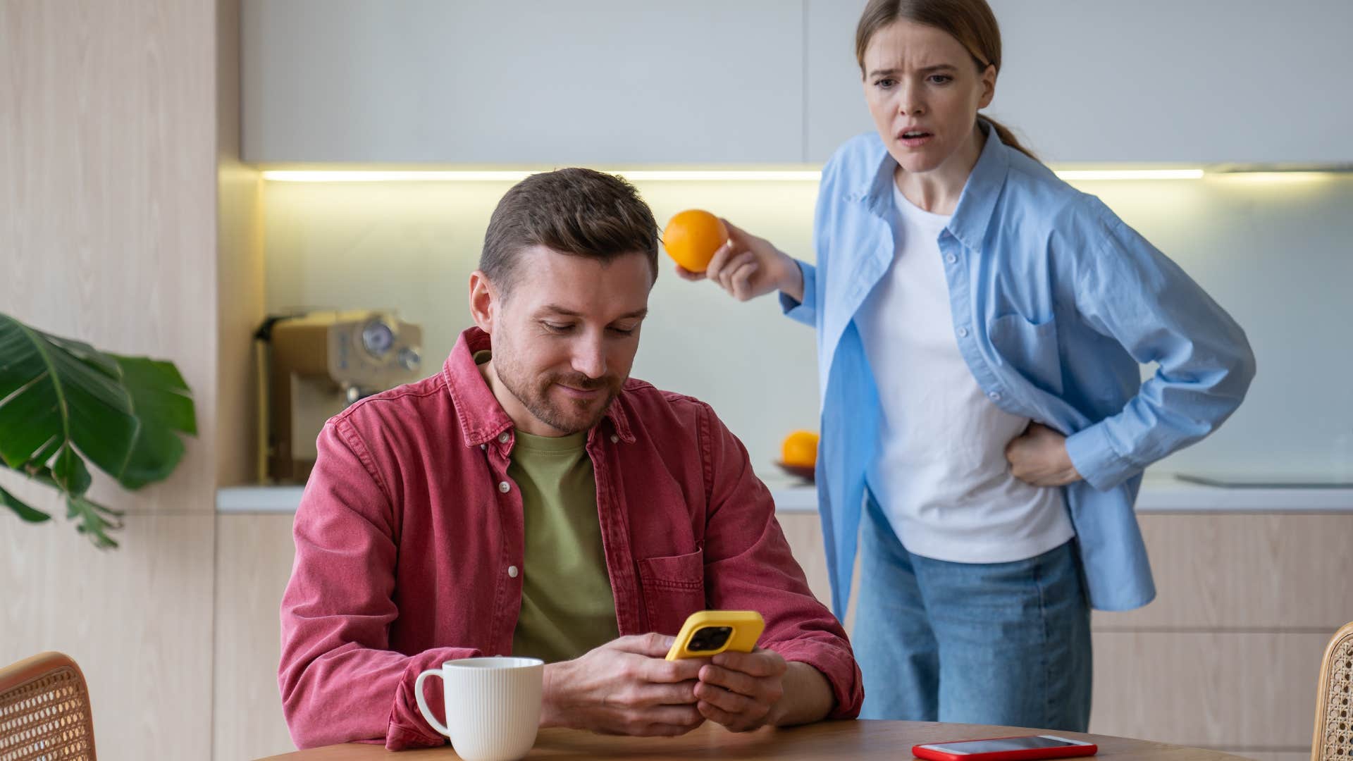 Man smiling at his phone while a woman looks angrily at him. 