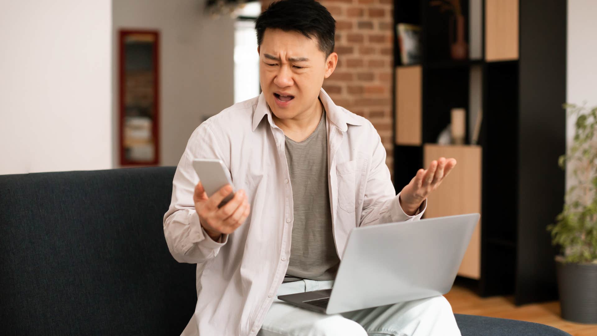 Man looking angry at his laptop and cell phone.