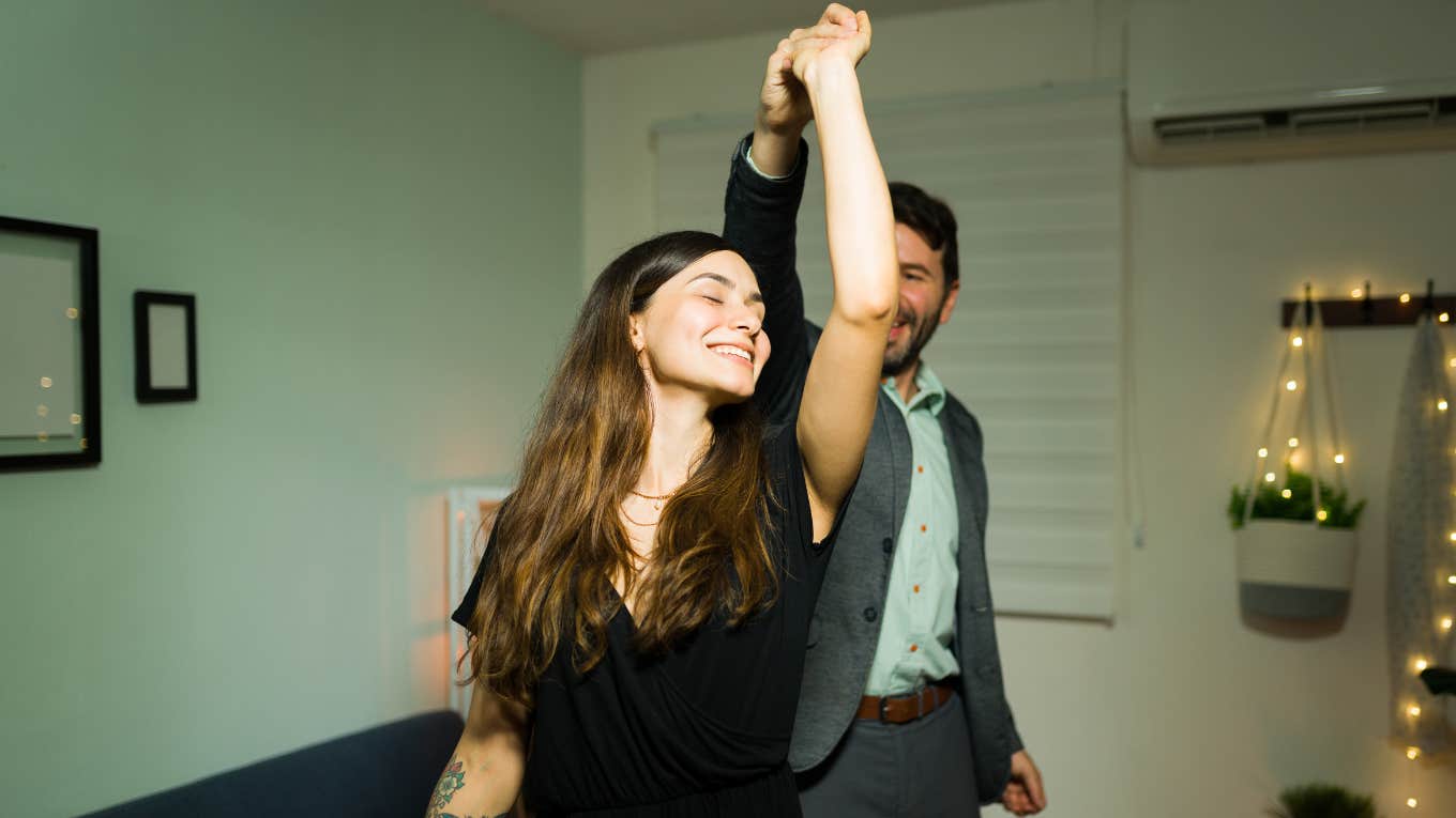 Beautiful young woman enjoying a slow dance with her husband in their living room home 