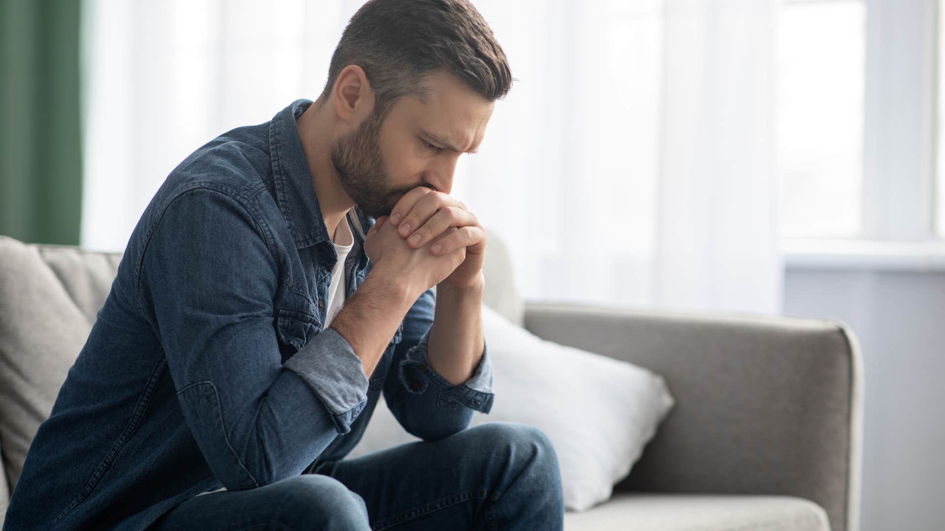 Adult man looking upset sitting on his couch.