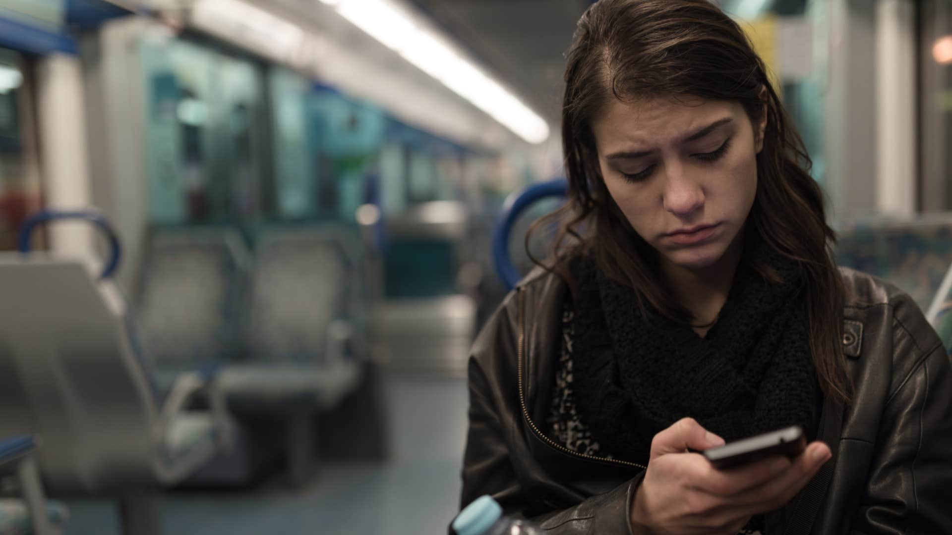 Woman looking sad on a bus staring at her phone.