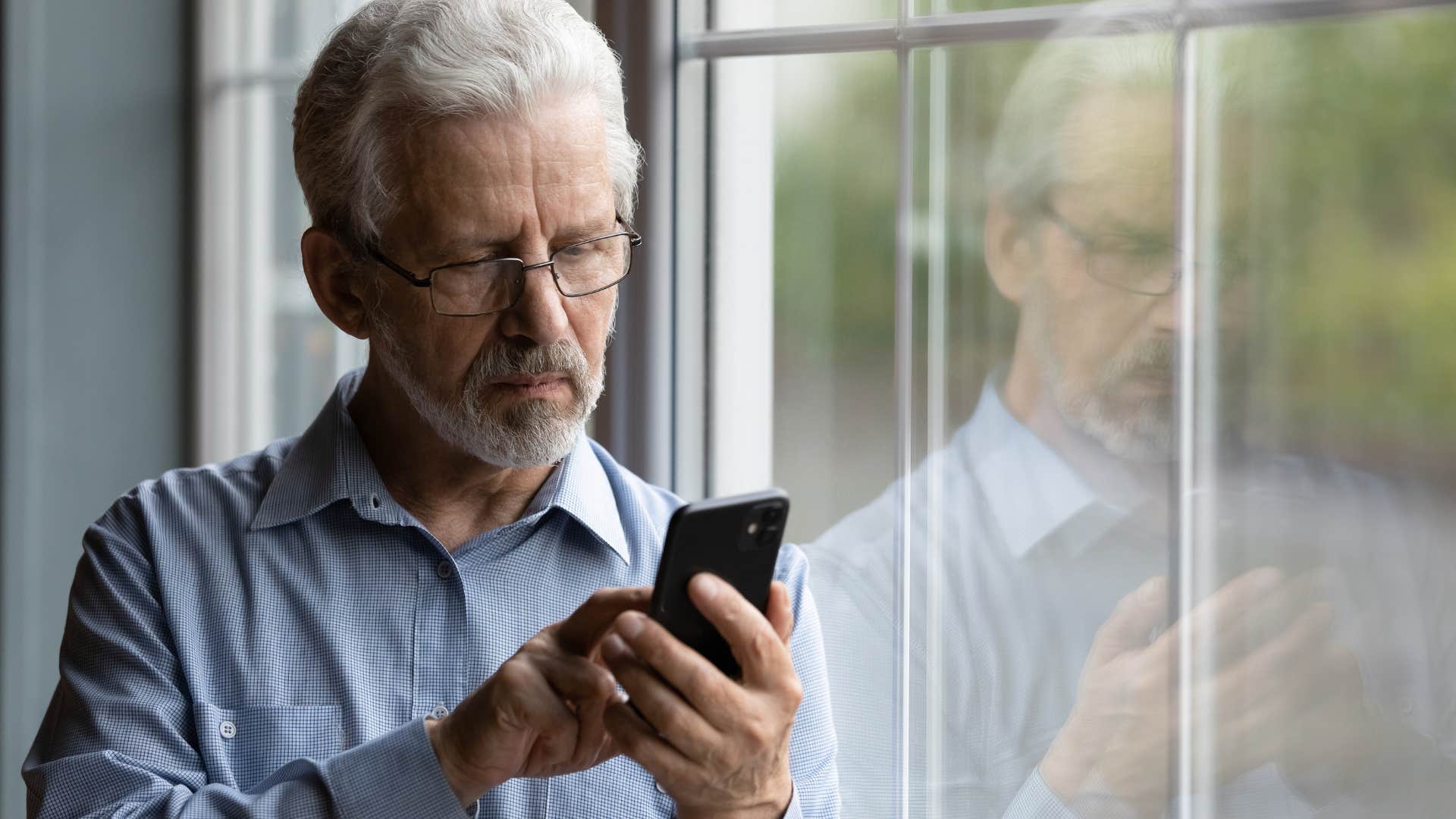 Older man looking sad staring at his phone.