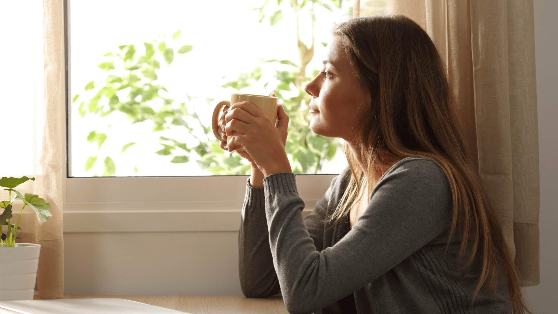 woman drinking hot drink and looking out the window