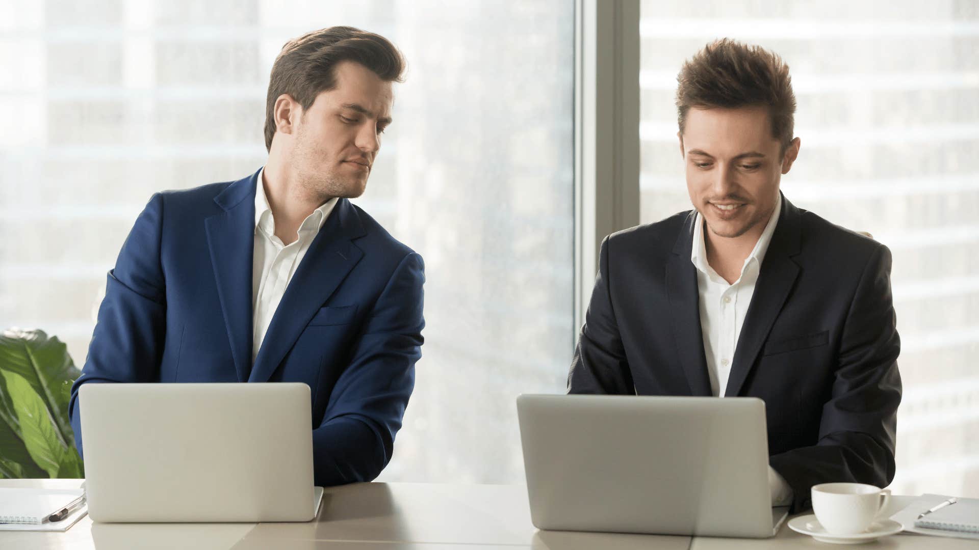 man curiously looking at other man's laptop