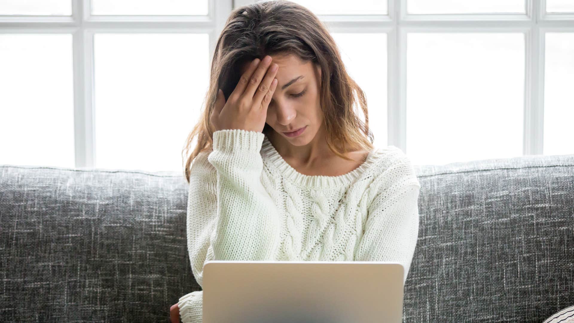 Tired woman looking at her laptop on the couch.