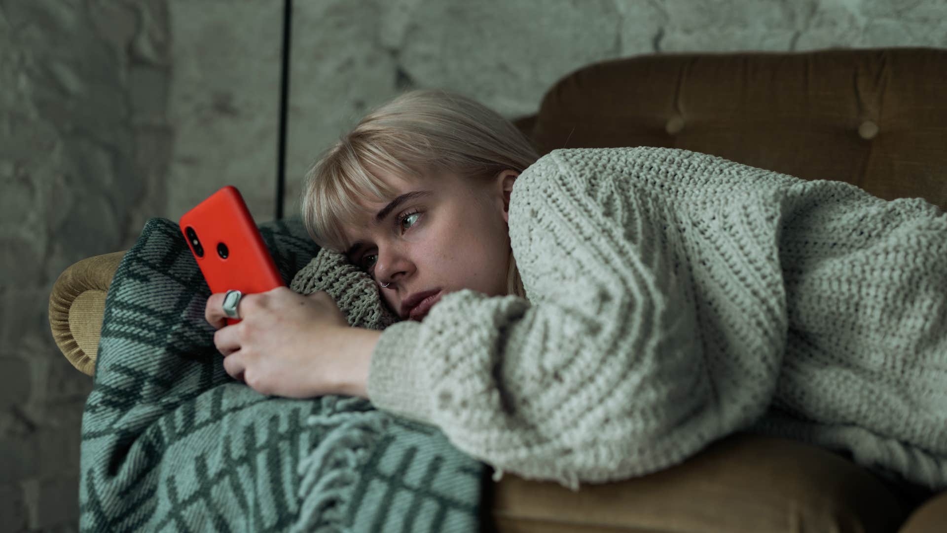 Woman looking sad laying in her bed on her phone.