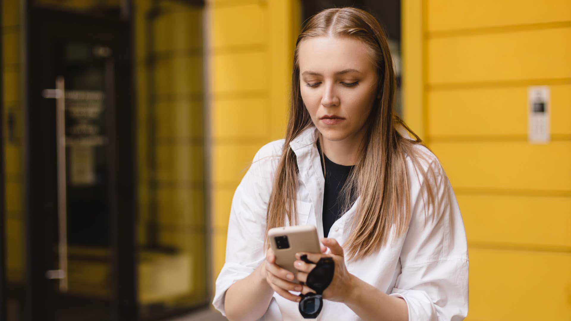 Woman sadly typing on her phone in public.