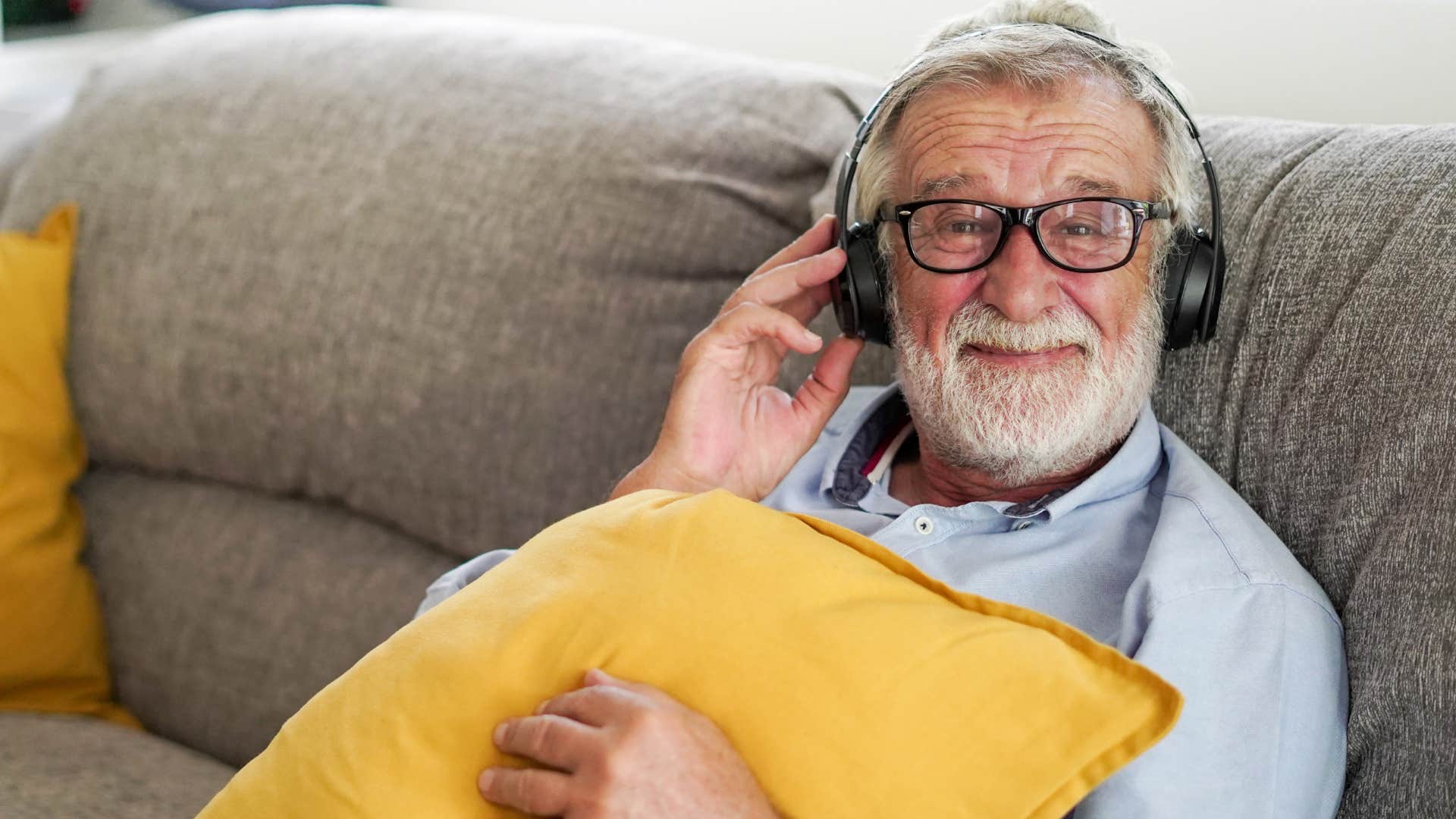 Older man smiling and listening to music on the couch.