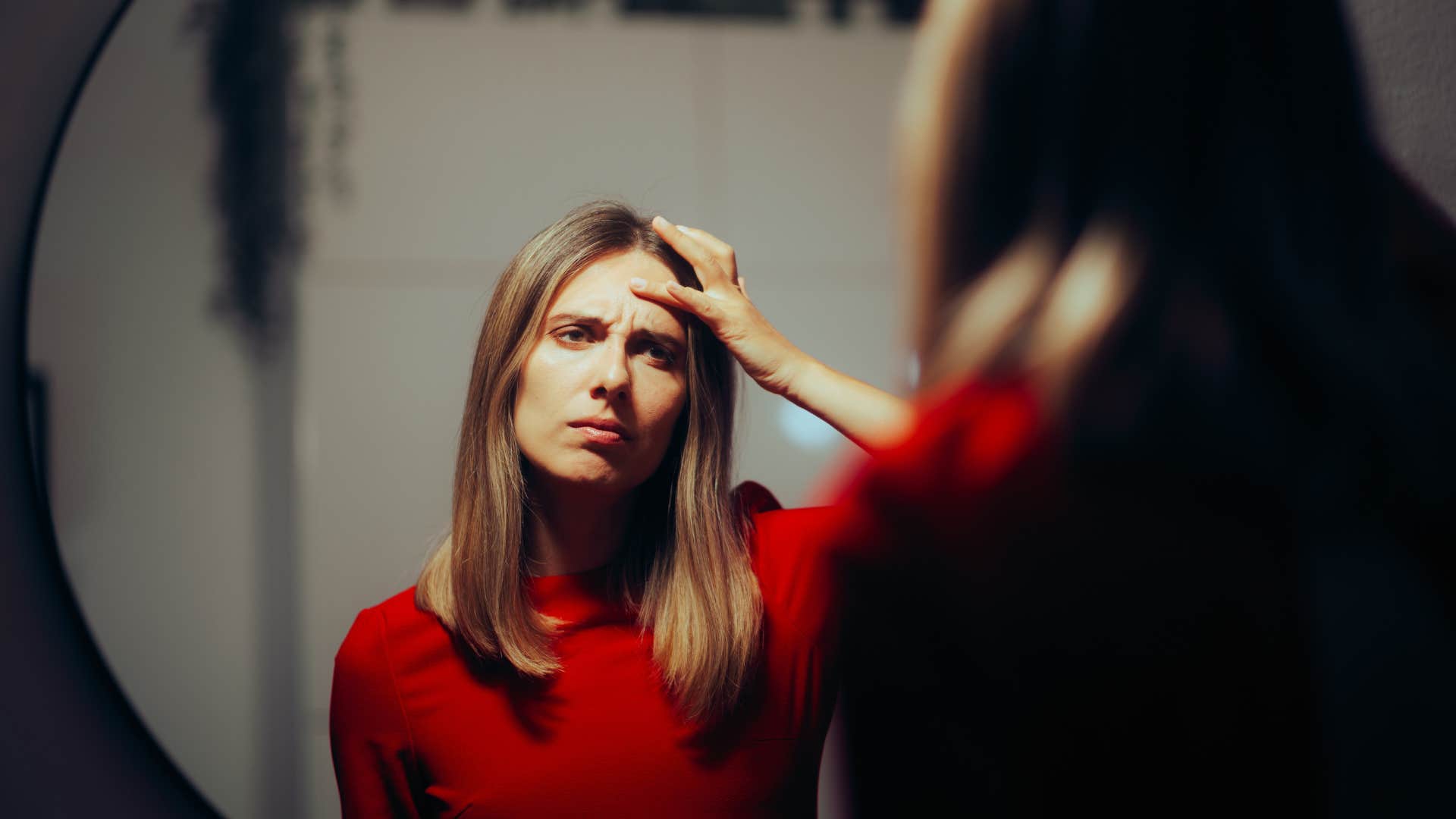 Woman looking upset staring in a mirror.