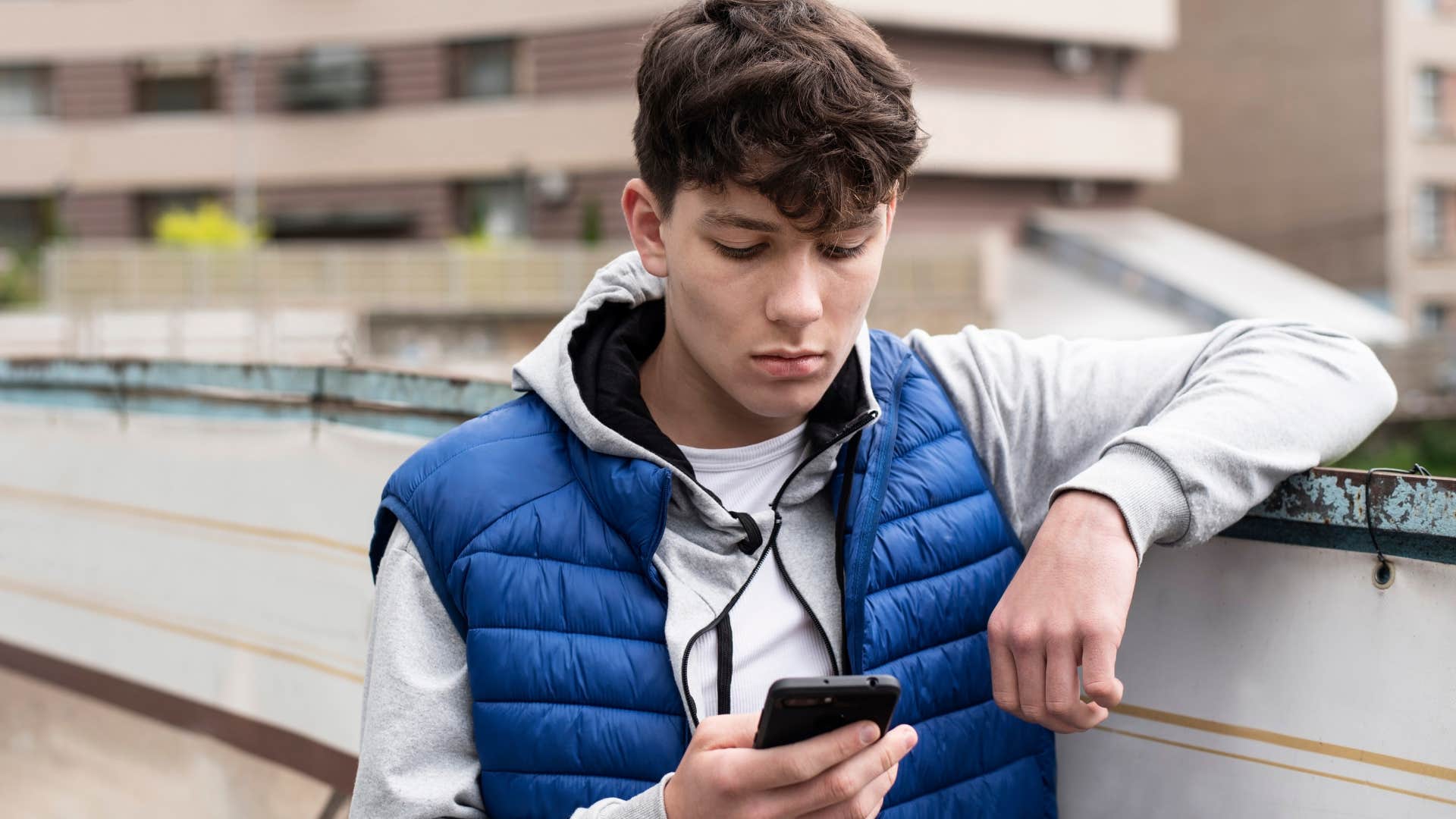 Teenage boy looking sad staring at his phone.