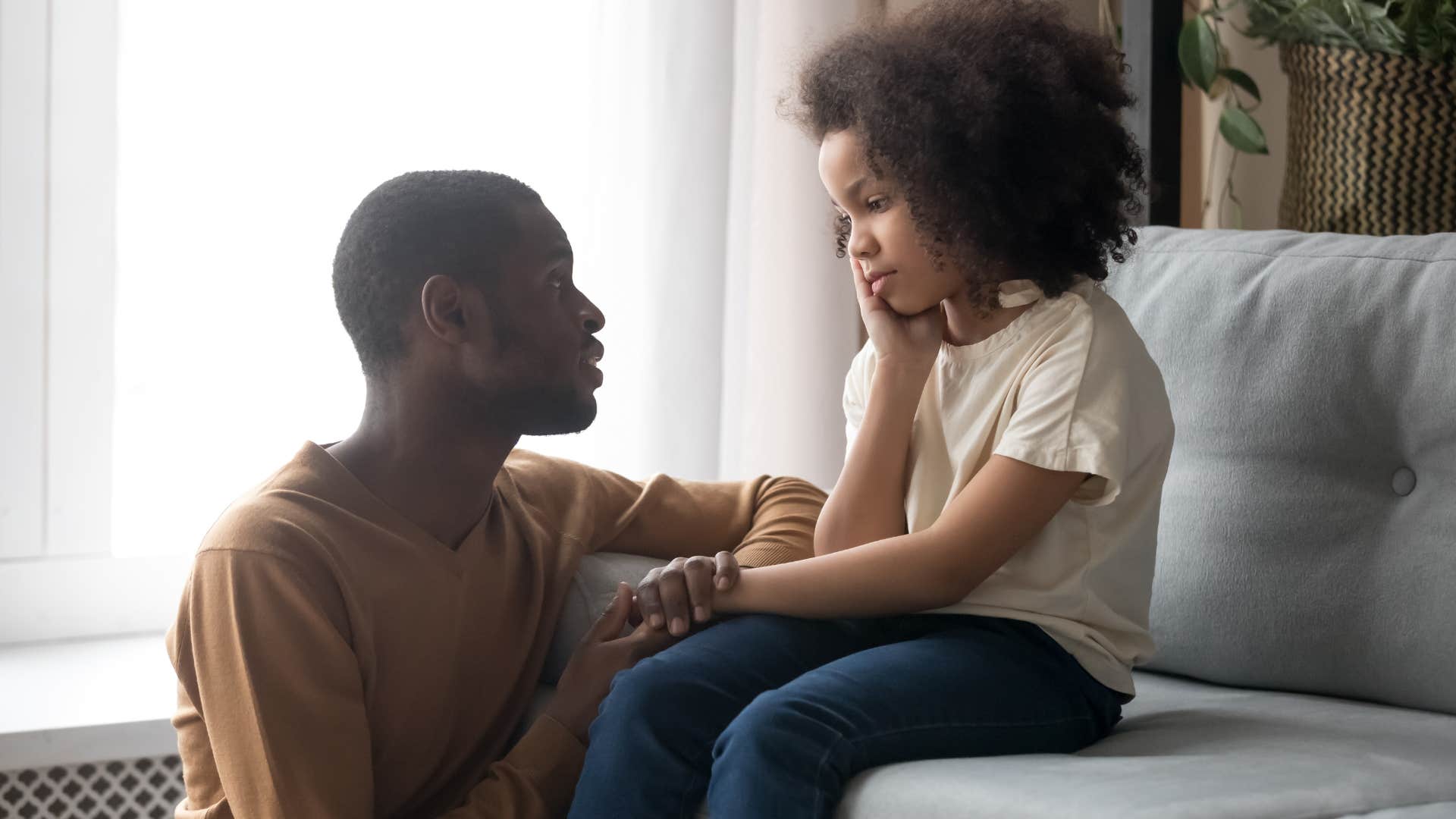 Dad talking to his young daughter on the couch.