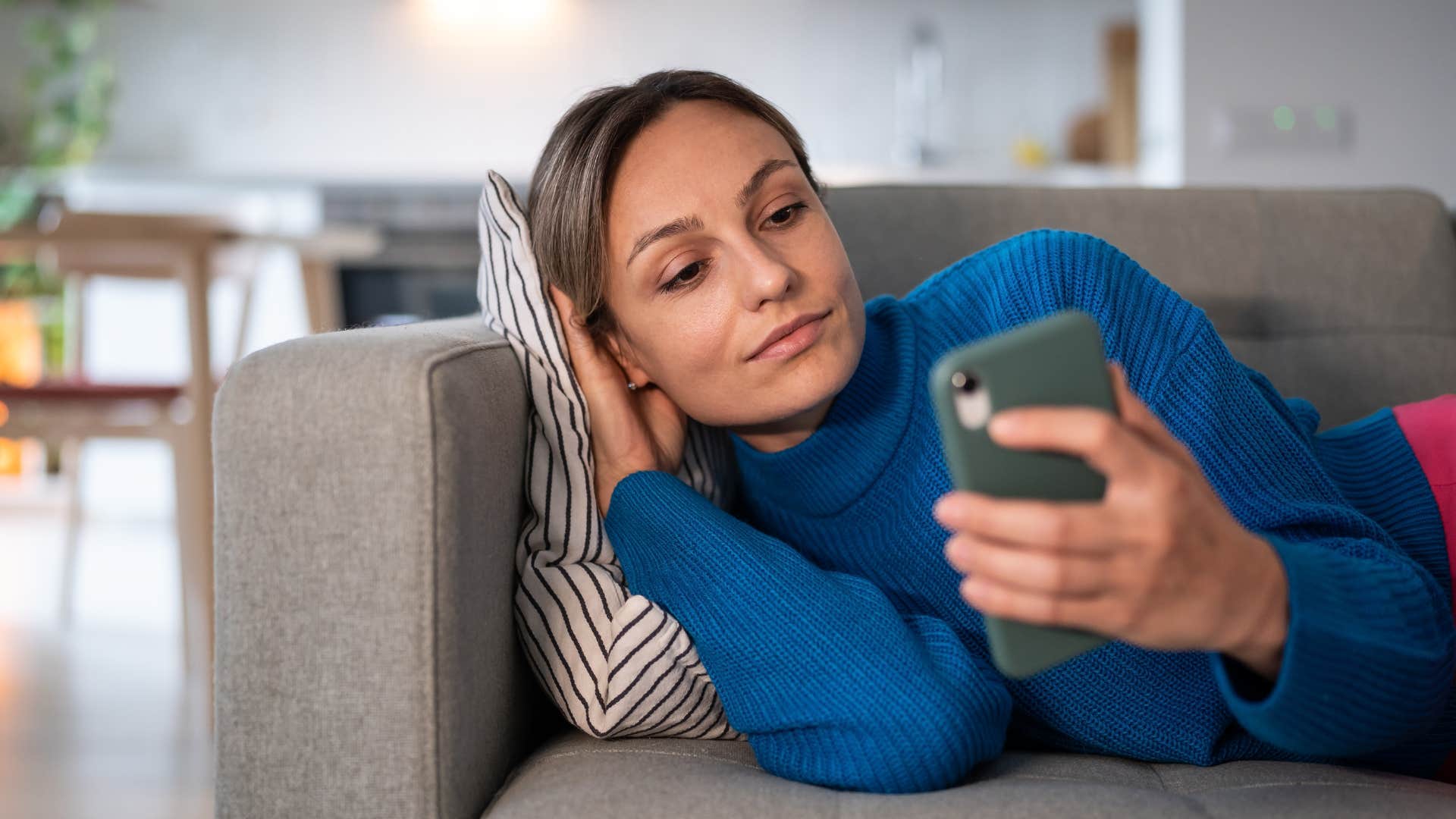 Woman looking calm staring at her cell phone on the couch.