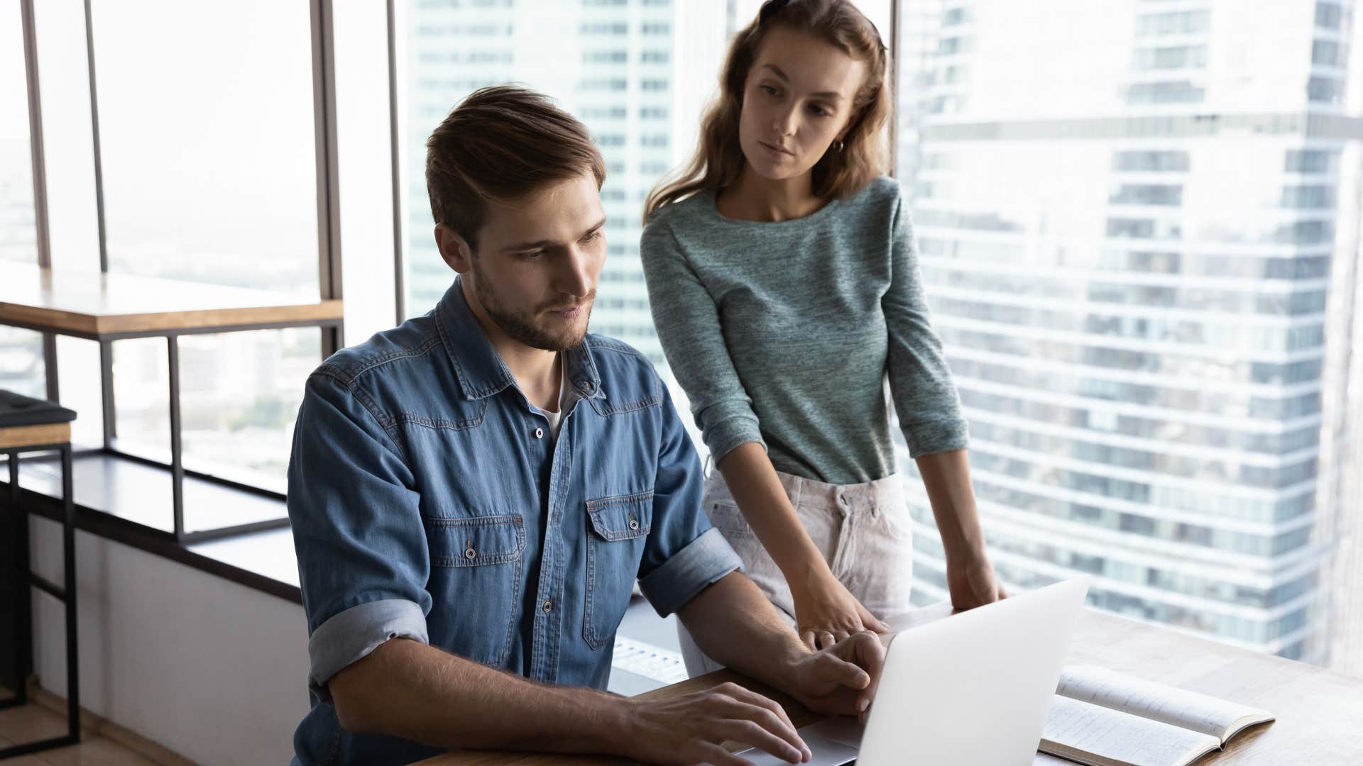 Woman standing over a male employee and watching his laptop. 