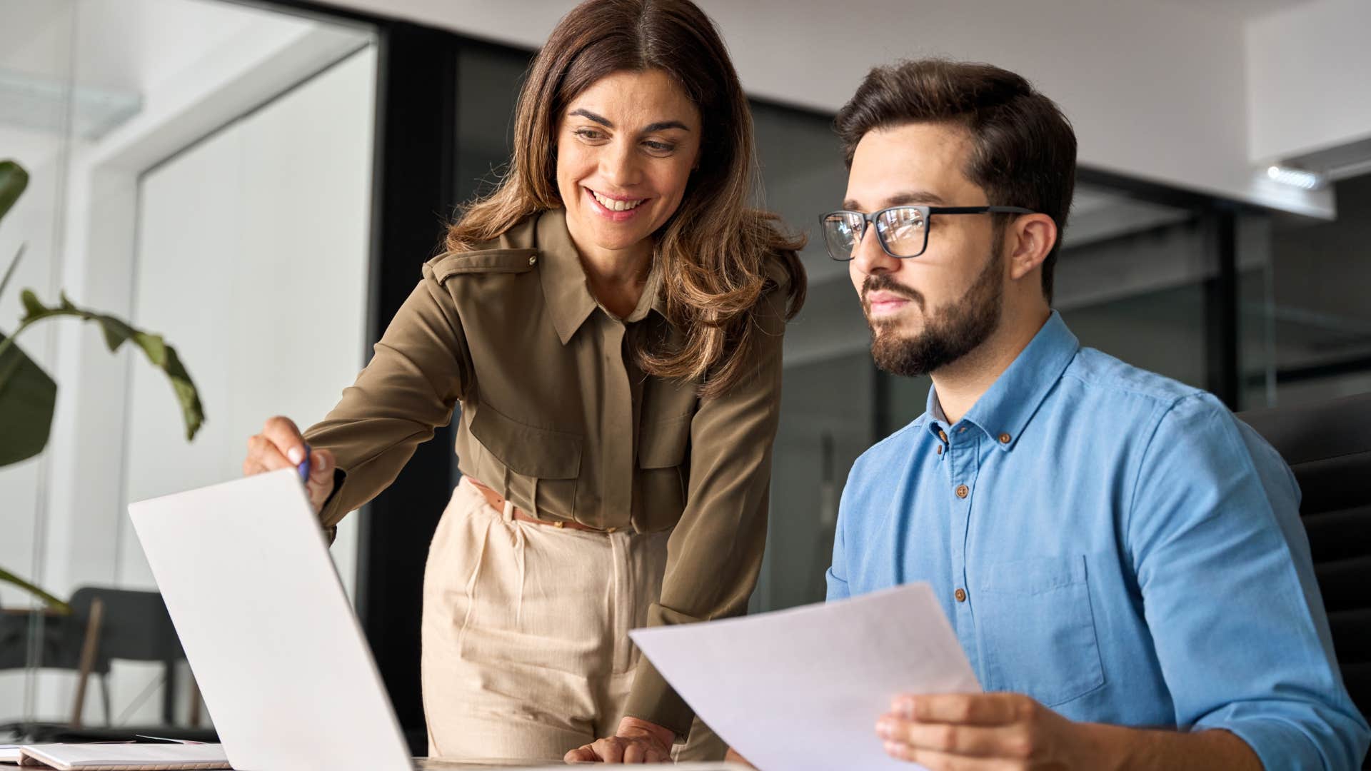 Female boss pointing at an employee's laptop and smiling.